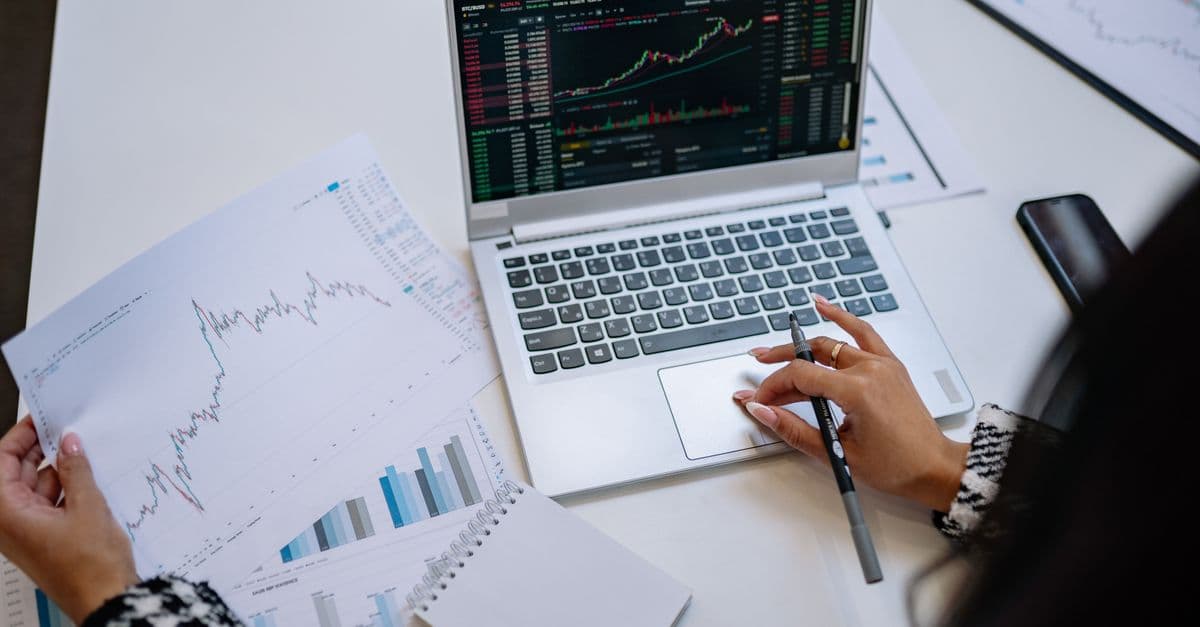 Financial charts displayed on a laptop beside printed analysis