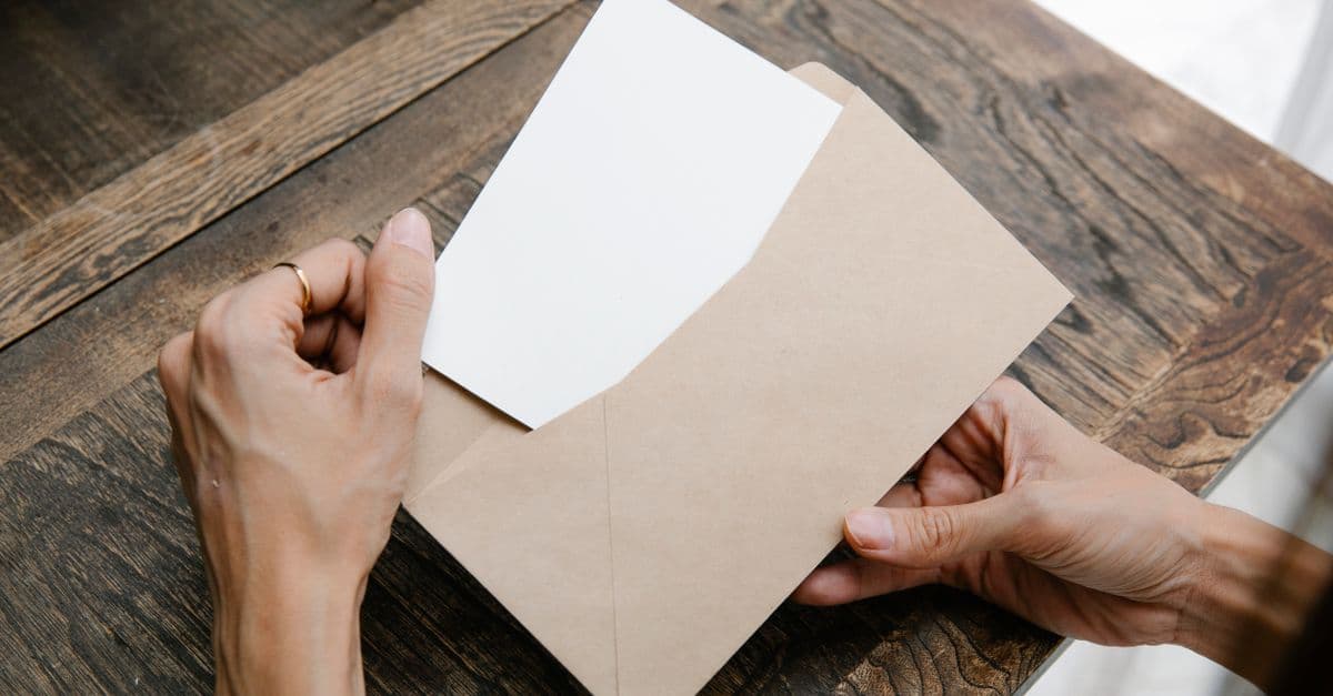 Hands opening a brown envelope with a white sheet of paper over a wooden table