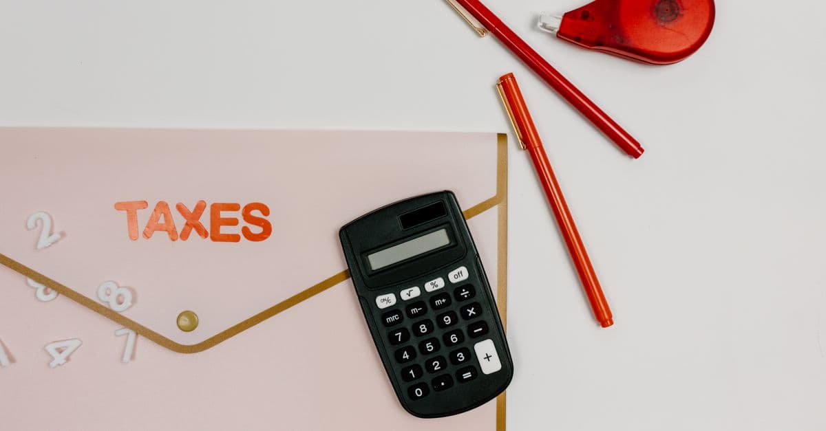 Calculator, red pens, and a folder labeled Taxes arranged on a desk
